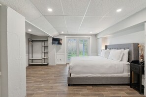 Un dormitorio con una cama grande, un televisor montado en la pared y un ventanal corredero que da a un balcón.