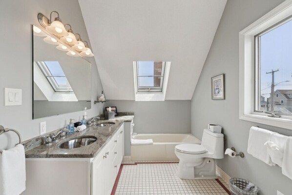 A modern bathroom with a skylight, a bathtub, a toilet, and a vanity with a sink.