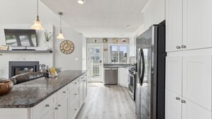 A modern kitchen with white cabinets, a granite countertop, stainless steel appliances, pendant lighting, and a large window. - Coastal Dream Vacation Home at Moody Beach - Sleeps 8 (Wells)