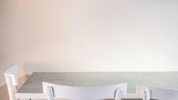 Une table à manger blanche avec des chaises, un mur de couleur claire et une étagère blanche au-dessus.
