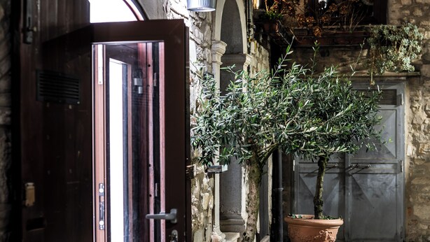 An open wooden door leading into a stone building with a potted olive tree and a large terracotta pot. - LA SUITE DEL CONVENTO (Potenza)