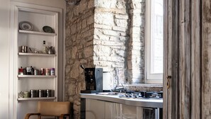 A kitchen with a stone wall, a wooden chair, and a window with curtains. - LA SUITE DEL CONVENTO (Potenza)
