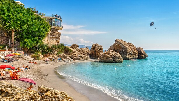 Uma praia com águas azuis cristalinas, formações rochosas e uma plataforma de observação.