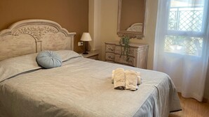Uma cama bem arrumada com cabeceira, uma mesa de cabeceira com abajur, um penteado com espelho e uma janela com vista.