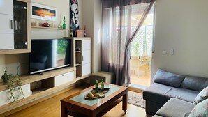 Uma sala de estar com televisão de tela plana, armários de madeira, mesa de centro de vidro e sofá cinza.