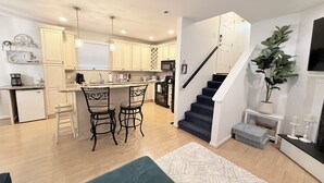 Un apartamento moderno con cocina, comedor y sala de estar. Incluye una escalera, un pequeño rincón de descanso y una planta en maceta.