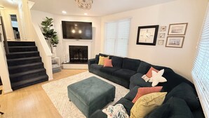 Una sala de estar con chimenea, un televisor grande y una escalera que sube a otro nivel.