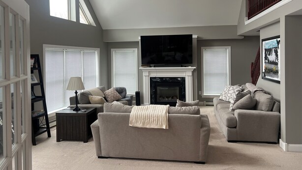 A spacious living room with a fireplace, two sofas, a TV, and large windows.