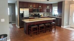 A modern kitchen with dark wood cabinets, stainless steel appliances, a central island with bar stools, and pendant lighting.