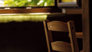 A wooden chair in a room with a window, a view of greenery outside, and a partial view of a window frame. - Rosemary House (Santiago do Cacém)