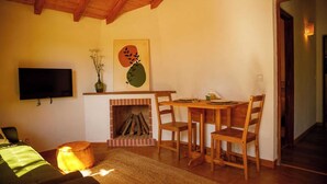 A cozy living room with a fireplace, a dining table, and a TV mounted on the wall. - Rosemary House (Santiago do Cacém)