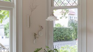 A corner room with a bay window, a small table with a potted plant, two white chairs, and a hanging light fixture. - Magnolia Tree - One Bedroom Apartment, Sleeps 2 (Bergen)