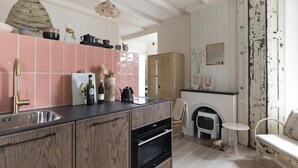 A modern kitchen with pink tiles, a wooden cabinet, a hanging light, and a rustic fireplace. - Magnolia Tree - One Bedroom Apartment, Sleeps 2 (Bergen)