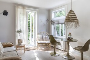 A bright room with a large window, a round table, two chairs, a lamp, and a chair with a cushion.