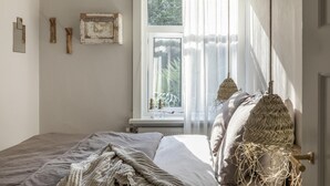 Een slaapkamer met een bed, een raam met dunne gordijnen en decoratie aan de muur.