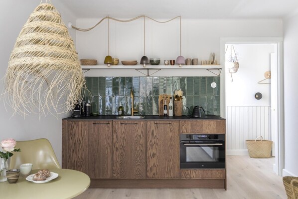 A modern kitchen with wooden cabinets, a built-in oven, and a hanging light fixture.