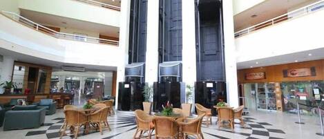 Een ruime lobby met een geruit vloertapijt, verschillende zithoeken en een centrale trap.