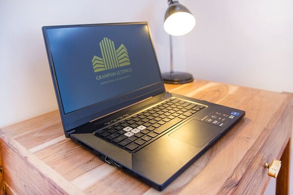 Una computadora portátil sobre una superficie de madera, con un logotipo en la pantalla, una lámpara de escritorio y una llave al lado.