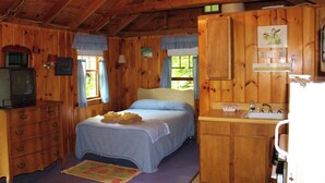 Un dormitorio de cabaña de madera con cama, cómoda y una pequeña kitchenette.