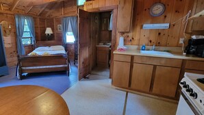 Una cabaña de madera con una cama, una pequeña kitchenette y un comedor.