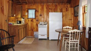 Una cocina con paneles de madera, que incluye un horno, un refrigerador y una mesa de comedor con sillas.