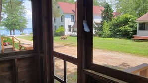 Vista desde una ventana que da a un patio trasero con una terraza de madera, una mesa de picnic y una casa con techo rojo.