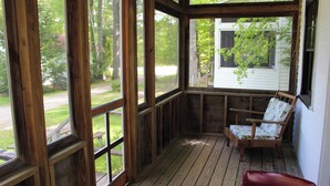A wooden porch with large windows, a wooden bench, and a chair. - Birch Cottage-Private Beach-Pets Welcome - Round Table Lodge, Sebago, Maine (Sebago)