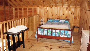 A wooden cabin bedroom with a bed, a small table with towels, and a dresser. - Birch Cottage-Private Beach-Pets Welcome - Round Table Lodge, Sebago, Maine (Sebago)
