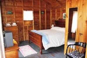 Un dormitori de cabana de fusta amb un llit, una petita arca i una cadira.