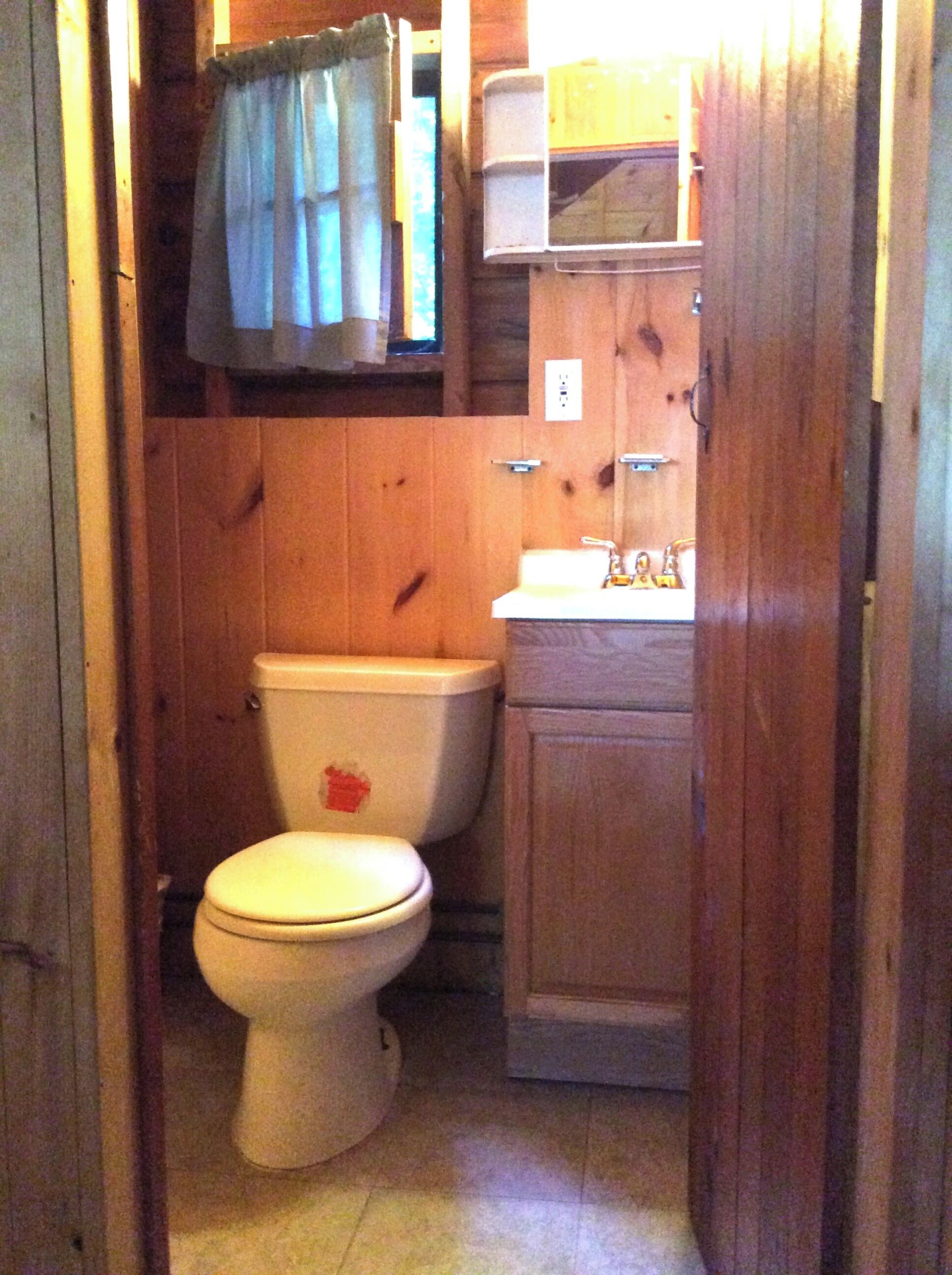 A small, wooden bathroom with a toilet, sink, and cabinet.