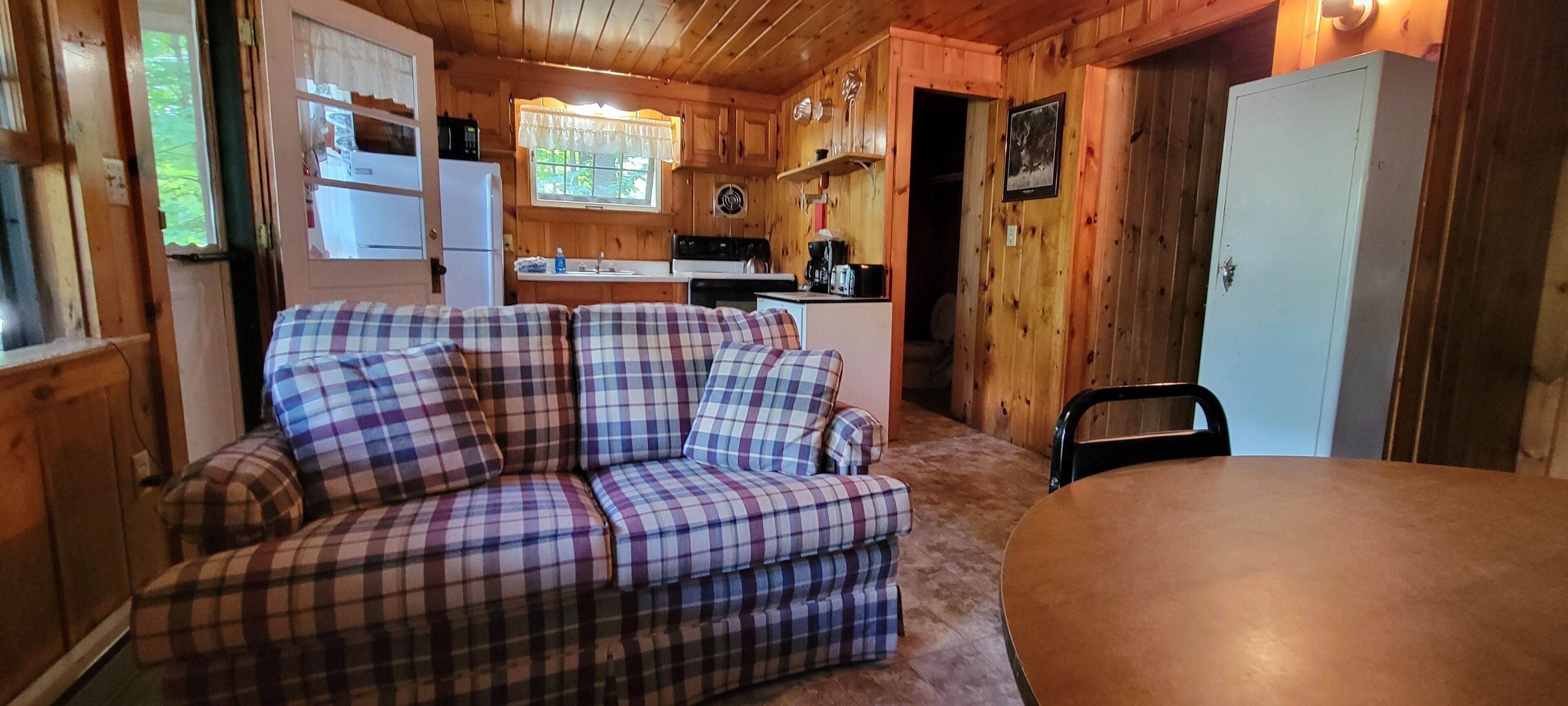 Acogedor interior de cabaña con sofá de cuadros, una mesa de comedor, una zona de cocina y paredes de madera.