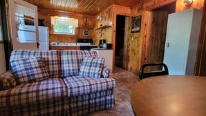 En mysig stuga med en soffa i rutigt tyg, ett matbord, ett köksutrymme och väggar i trä.