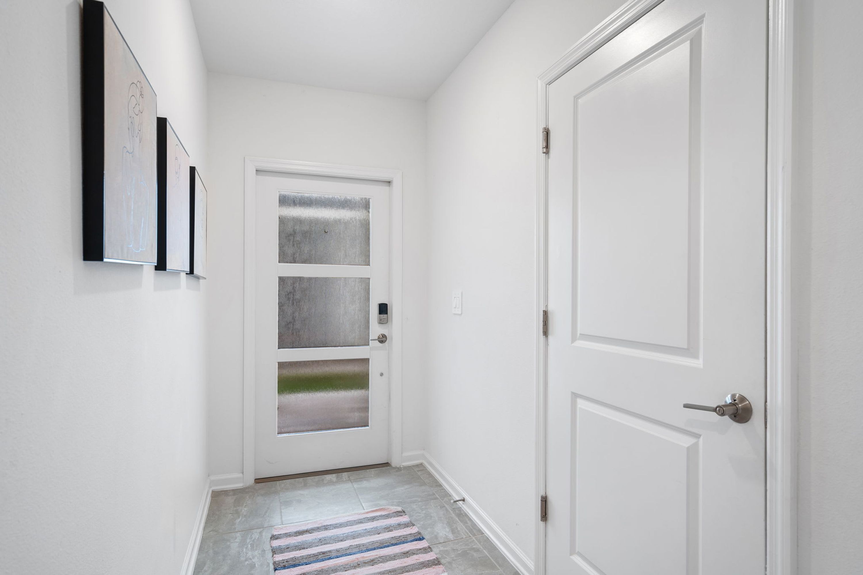 Un couloir avec une porte blanche, un tapis à rayures et trois œuvres d’art encadrées accrochées au mur.