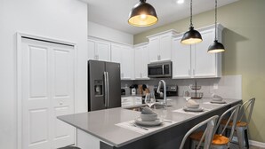 A modern kitchen with white cabinets, stainless steel appliances, and a central island with bar stools. - Condo 2bed 2bath Next to Disney w Free Water Park (Davenport)