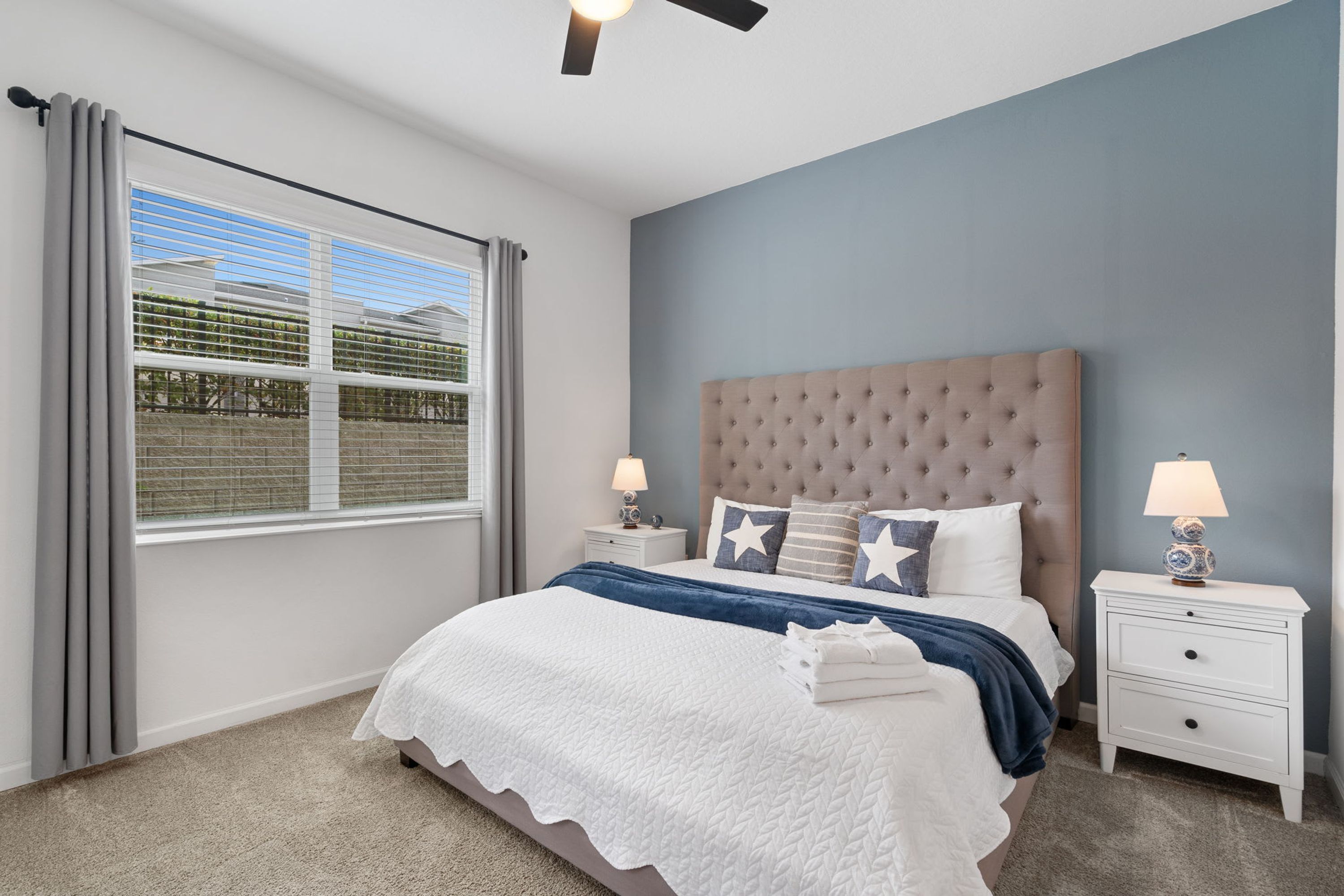 A bedroom with a large bed, two bedside tables, a ceiling fan, and a window with blinds.