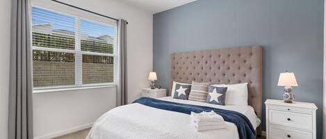 A bedroom with a large bed, two bedside tables, a ceiling fan, and a window with blinds.