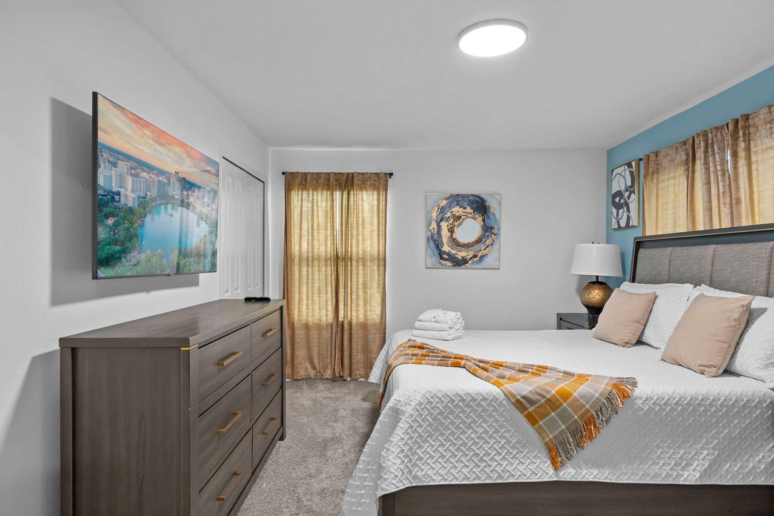 A bedroom with a bed, a dresser, a nightstand, a lamp, and artwork on the walls.