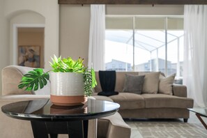Un salon moderne avec une table ronde en verre, un canapé beige et une grande fenêtre avec des rideaux.