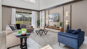 A spacious living area with a large window, a sofa, a blue armchair, and a coffee table. - Chic 5bed Home Close to Disney Parks (Davenport)