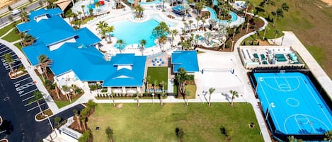 Vista aérea de un complejo turístico con una gran piscina, cancha de baloncesto y aparcamiento.