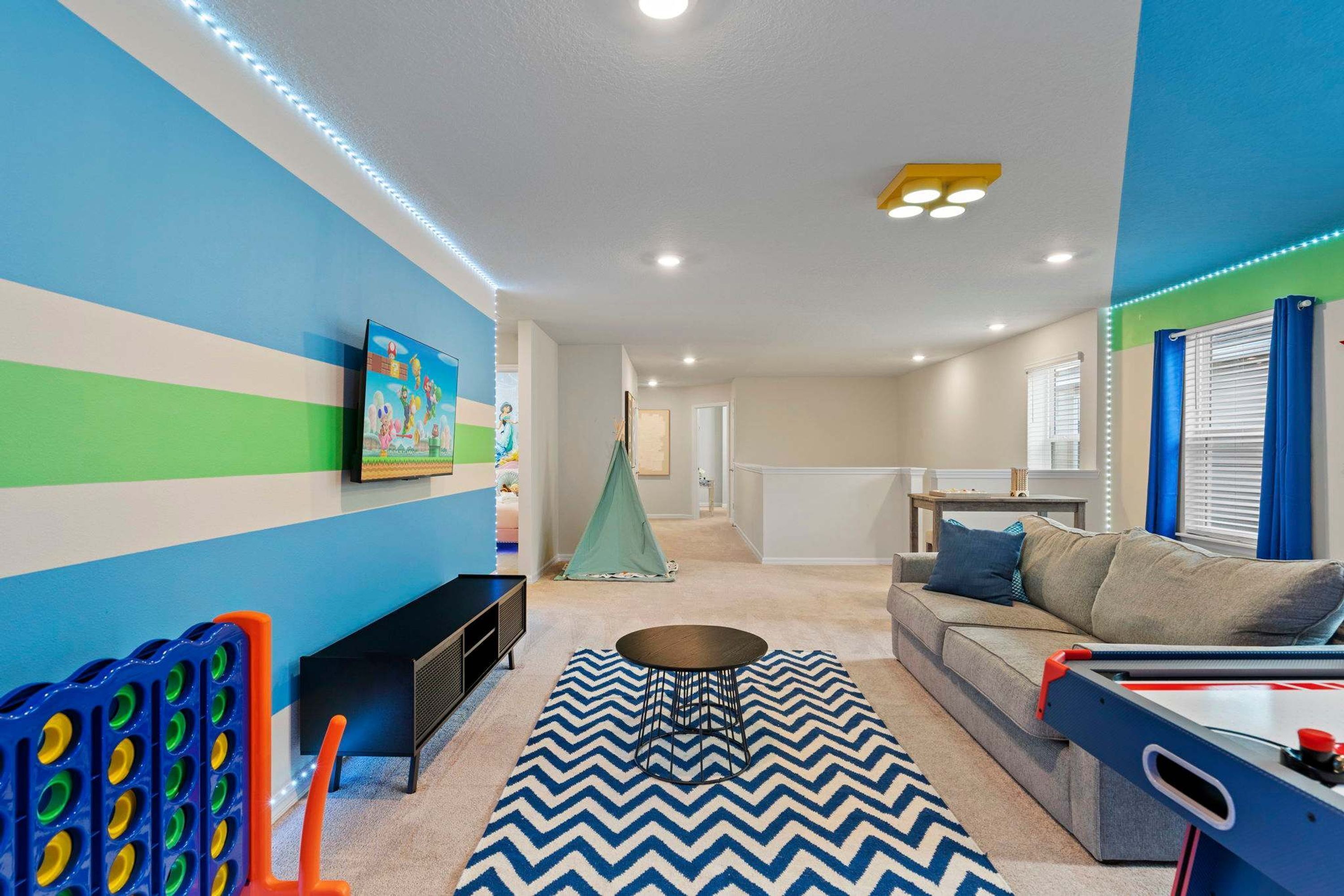 Una habitación con un tapete de diseño azul y blanco a rayas de chevrón, una tienda verde, un sofá con cojines azules y una mesa de ping pong.