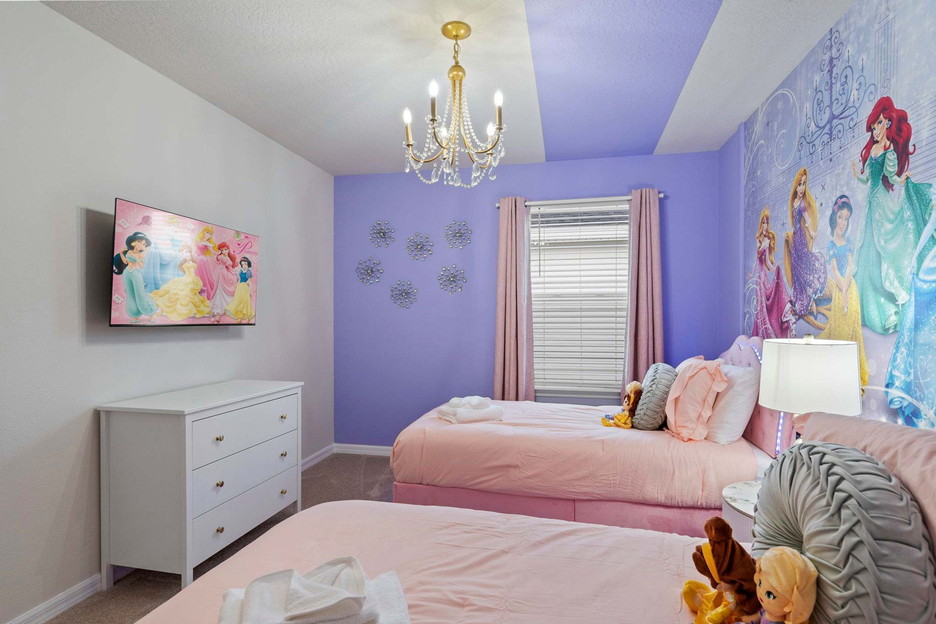 A bedroom with two beds, a dresser, a chandelier, and a mural on the wall.