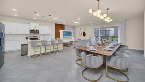 A modern kitchen with white cabinets, a central island, and a dining area with a long table and chairs.