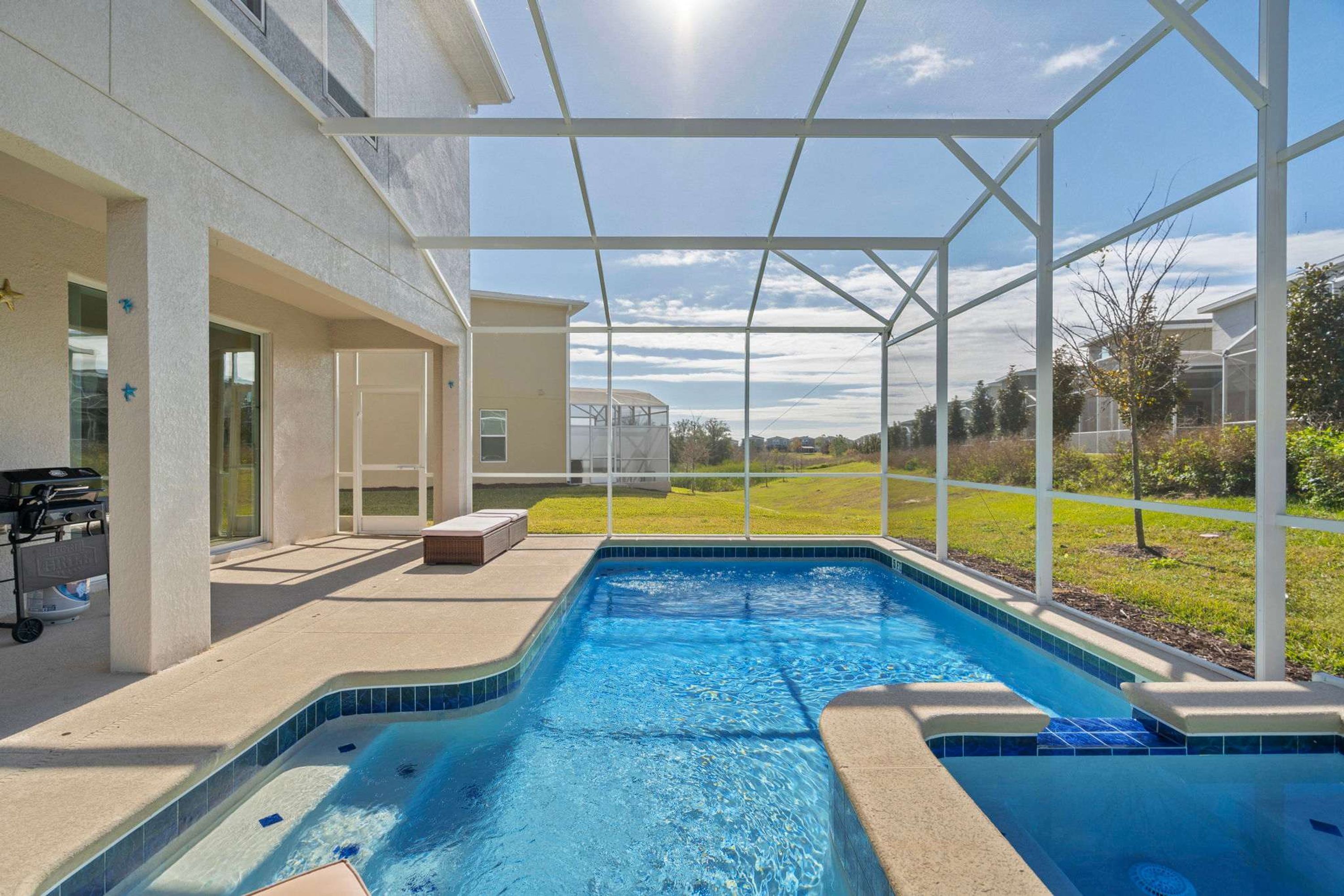 A swimming pool with a covered area, a patio with a grill, and a view of a residential neighborhood.