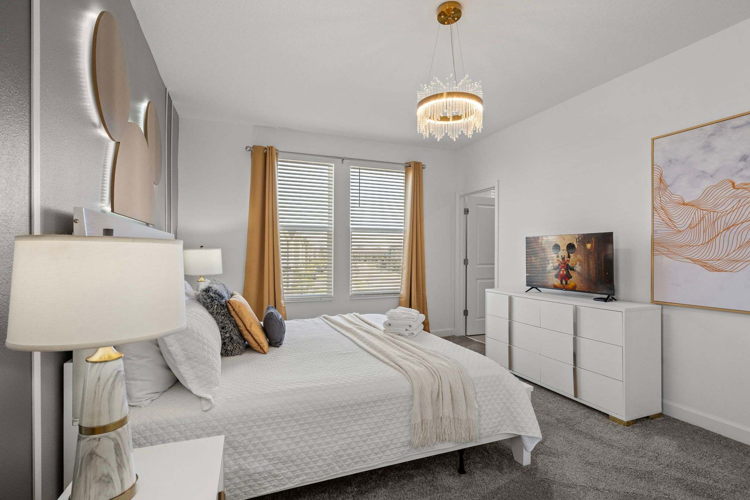 Ein modernes Schlafzimmer mit Bett, Nachttischlampe, Fernseher und Kunstwerken.