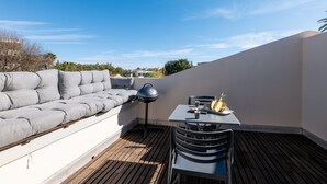 Eine Dachterrasse mit einer grauen Couch, einem Tisch mit Grill und einem Stuhl.