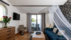 Ein modernes Wohnzimmer mit Couchtisch aus Holz, einem blauen Sofa, einem grauen Sessel, einer Holzkommode und einem an der Wand montierten Fernseher.