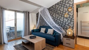 Een moderne woonkamer met een blauwe bank, een houten salontafel en een glazen deur naar een buitenruimte.