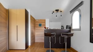 Een compacte keuken met een centraal eiland, twee barkrukken en een houten garderobe.