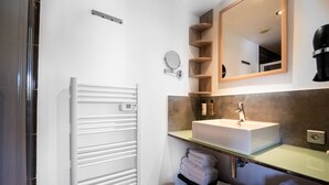 A modern bathroom with a white radiator, a sink with a mirror above, and wooden shelves. - Top Floor Studio Le Nid d’Amour Mandara Beach (Antibes)